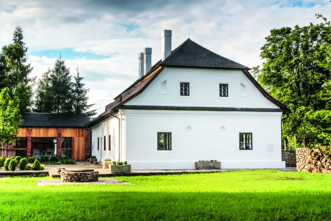 Citlivě zrekonstruovaný venkovský dům u lesa s bílou fasádou a šindelovou střechou