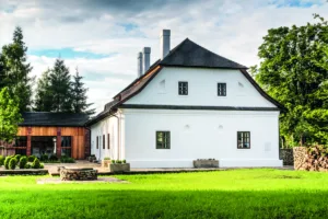 Citlivě zrekonstruovaný venkovský dům u lesa s bílou fasádou a šindelovou střechou