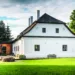 Citlivě zrekonstruovaný venkovský dům u lesa s bílou fasádou a šindelovou střechou